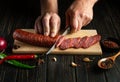 Chef cuts veal sausage on a wooden cutting board. Cooking delicious sandwiches for dinner on the kitchen table at home. Copy space Royalty Free Stock Photo