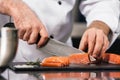 Chef cutting fish fillet. Closeup chef hands cut salmon at kitchen table. Royalty Free Stock Photo