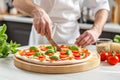 Chef cutting pizza with knife on wooden board in kitchen, close up Royalty Free Stock Photo