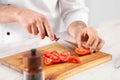 Chef cutting tomatoes at marble table in kitchen, closeup