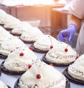 A chef decorates cakes in a confectionery factory with fresh cherry. Dessert mass production, background, industry Royalty Free Stock Photo