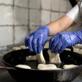 Chef dipping raw dough in boiling oil. Fresh baking, cooking process. Cook in disposable gloves fries pieces of dough in