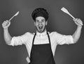 Chef with excited face holds wooden spoon and spatula on red background. Kitchenware and cooking concept. Man in Royalty Free Stock Photo