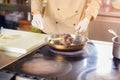 Chef frying shanks of lamb in frying pan.