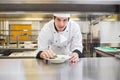 Male chef wearing chef jacket leaning over countertop in kitchen, adding garnishes to salad bowl Royalty Free Stock Photo