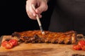 The chef gets BBQ sauce on ready-to-eat pork ribs lying on an old wooden table. A man prepares a snack to beer on a black backgrou Royalty Free Stock Photo