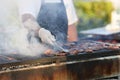 Chef grills cuts of meat on barbeque in smoke outside.