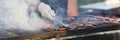 Chef grills cuts of meat on barbeque in smoke outside.