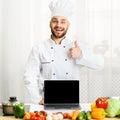 Chef Guy Holding Laptop Gesturing Thumbs-Up Standing In Kitchen Royalty Free Stock Photo