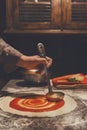 Chef hand spreading tomato paste on pizza base