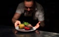 Chef handing plate with meal through order station in the commercial kitchen on black background.