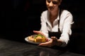 Chef handing plate with meal through order station in the commercial kitchen on black background.