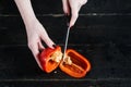 Chef hands cut red bell pepper on black wooden background. Royalty Free Stock Photo