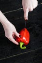 Chef hands cut red bell pepper on black wooden background. Royalty Free Stock Photo