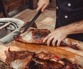 Chef Hands cutting whole grilled lamb for steaks with knife on cutting board. Hot Meat dishes.