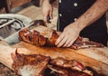 Chef Hands cutting whole grilled lamb for steaks with knife on cutting board. Hot Meat dishes