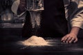 The chef hands are dropping flour over a wooden table