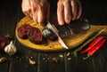 Chef hands with a knife cut blood sausage on a kitchen cutting board. Cooking a national dish with spices and pepper at home in Royalty Free Stock Photo