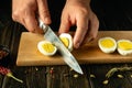 Chef hands and knife cutting a boiled egg in the kitchen for cooking or catering food. Gourmet meal concept on kitchen table in Royalty Free Stock Photo