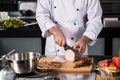 Chef hands with knife slice meat at kitchen. Closeup chef hands cutting hum.