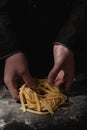 Chef hands making spaghetti, pasta, noodles with fresh pasta on black table with