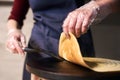 Chef hands turn over crepe with spatula helping on portable cooktop. Baking process. Blurred background. Close up view.