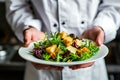 A chef is holding a plate of salad with a variety of vegetables and croutons Royalty Free Stock Photo