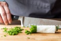 Chef holding a sharp knife behind a bundle of chives with some freshly chopped