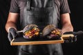 Chef holding two big, fresh grilled burgers with a black bun ready to eat.