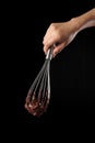 Chef holding wire whisk and melted chocolate on black background Royalty Free Stock Photo