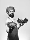 Chef holds bowl with potato casserole and vegetables. Man with beard on white background. Cook with proud face