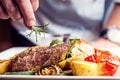 Chef in hotel or restaurant kitchen cooking only hands. Prepared beef steak with vegetable decoration Royalty Free Stock Photo