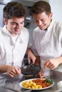 Chef Instructing Male Trainee In Restaurant Kitchen