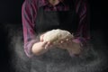 The chef keeps the dough and pours flour on a dark background. The concept of nutrition.