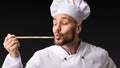 Chef Man Holding Spoon Tasting Food On Black Background, Panorama