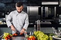 Chef man with knife at kitchen. Male professional cutting tomatoes.