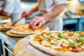 The chef in the pizzeria kitchen decorates a delicious pizza with mozzarella and basil