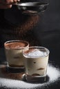 Chef pouring cacao on classic dessert tiramisu on glass