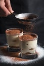 Chef pouring cacao on classic dessert tiramisu on glass