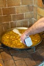 Chef pouring rice into the paella after cooking the first ingredients, for an authentic Valencian paella in a rustic kitchen with