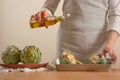 Chef pours olive oil and prepares to bake the artichoke on a light background, the concept of cooking tasty and healthy food, menu Royalty Free Stock Photo