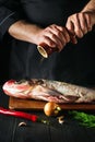 The chef prepares fresh fish bighead carp sprinkling pepper. Preparing to cook fish food. Working environment in restaurant or