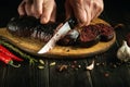 The chef prepares a national dish with spices at home. Blood sausage being cut by the hands of the cook on a kitchen cutting board Royalty Free Stock Photo