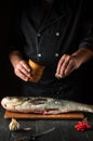 The chef prepares silver carp herring in the restaurant kitchen. The cook sprinkles salt on the fish. Work environment on the Royalty Free Stock Photo