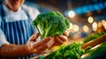 Chef presenting a fresh head of broccoli at a market stand with warm lights in the background Royalty Free Stock Photo