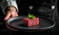 Chef presenting raw beef cube on black plate in restaurant background, copy space Royalty Free Stock Photo