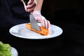 A chef in protective gloves puts a fried piece of red fish on a plate. White dishes. Unrecognizable person. Photo on a black