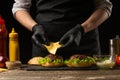 The chef puts the cheese on a burger, on the background of the ingredients.