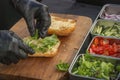 Chef puts lettuce leaves in a cut bun for making a burger or sandwich.