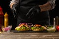 The chef puts marinated onions in rings on a burger, on the background of the ingredients. Horizontal photo, Tasty and unhealthy